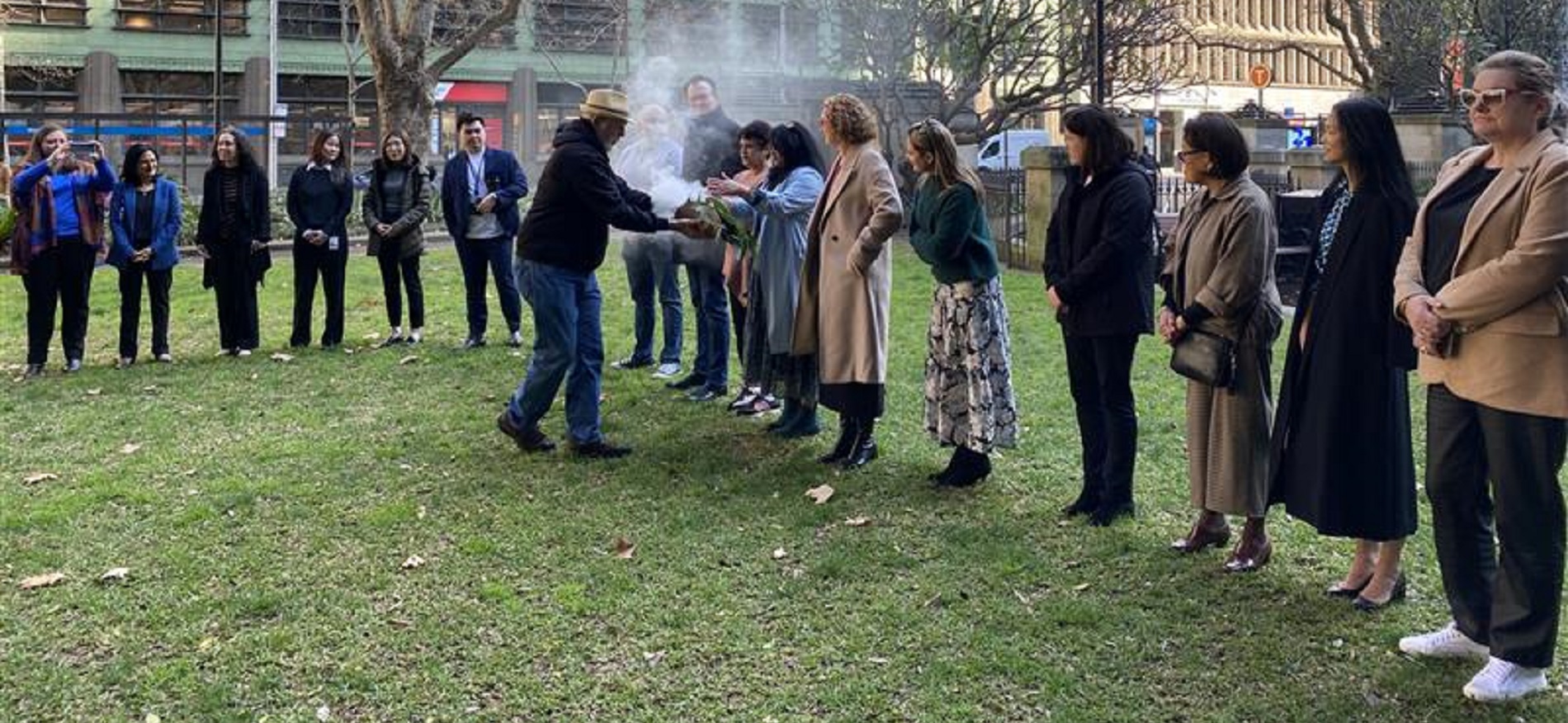 Row of people standing behind man as he carries out smoking ceremony