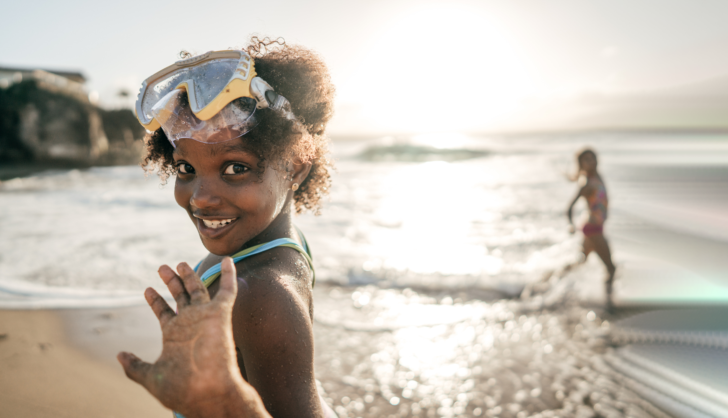 Child waving and smiling to camera while playing on beach